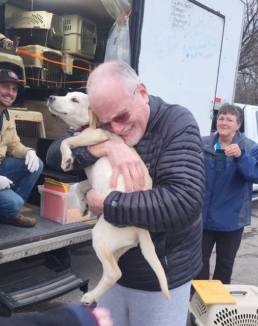 man standing smiling hugging a dog in his arms