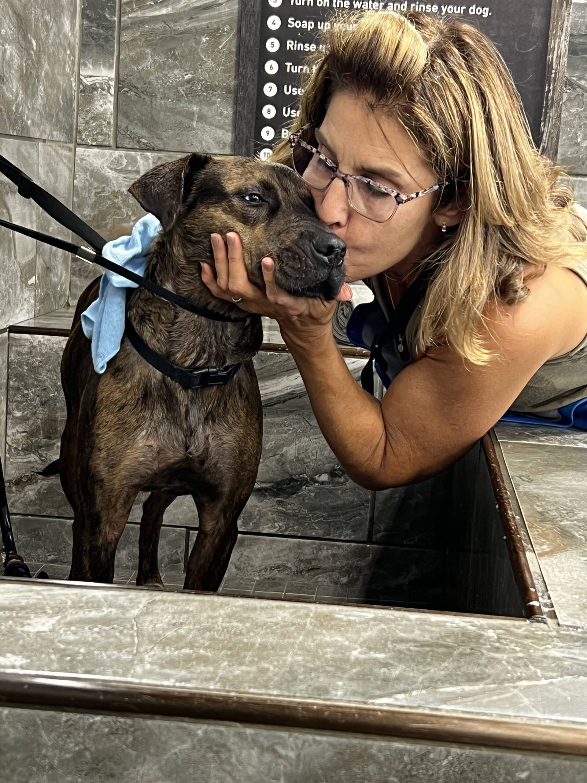 woman kissing a small dog in a bath stall