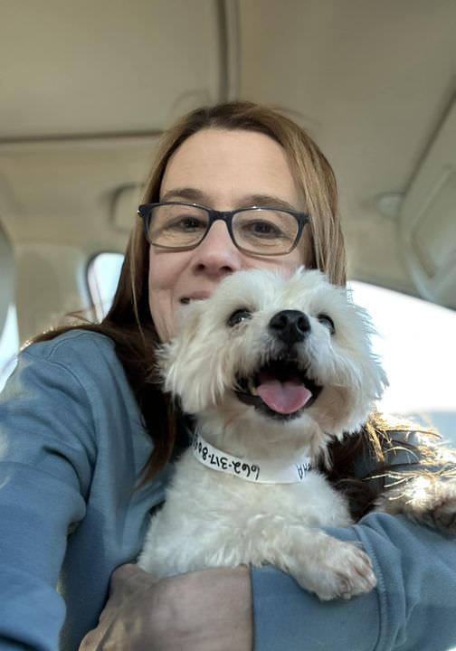 woman smiling holding a small white dog